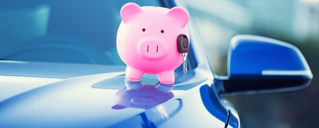 A pink piggy bank holding a car key sits on the hood of a blue car