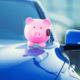 A pink piggy bank holding a car key sits on the hood of a blue car