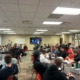 Director of Member Services Corey Olson stands at the front of a large classroom in filled with people sitting in chars at tables placed throughout the room.