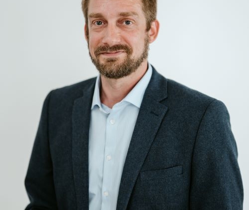 Cody Arendt headshot. Cody wears a dark blazer over a light-colored button-up shirt.